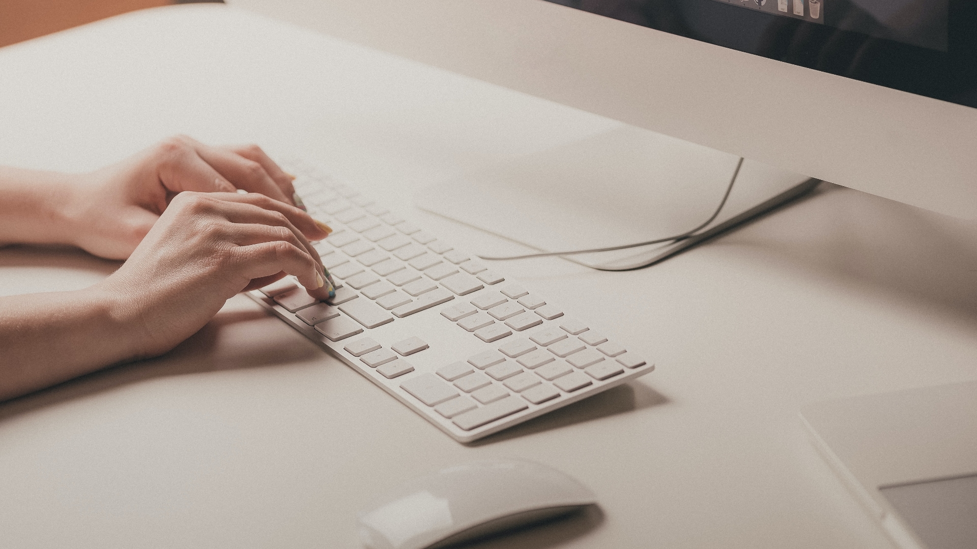 Caucasian person’s hands typing on a computer keyboard. A computer mouse is positioned nearby.