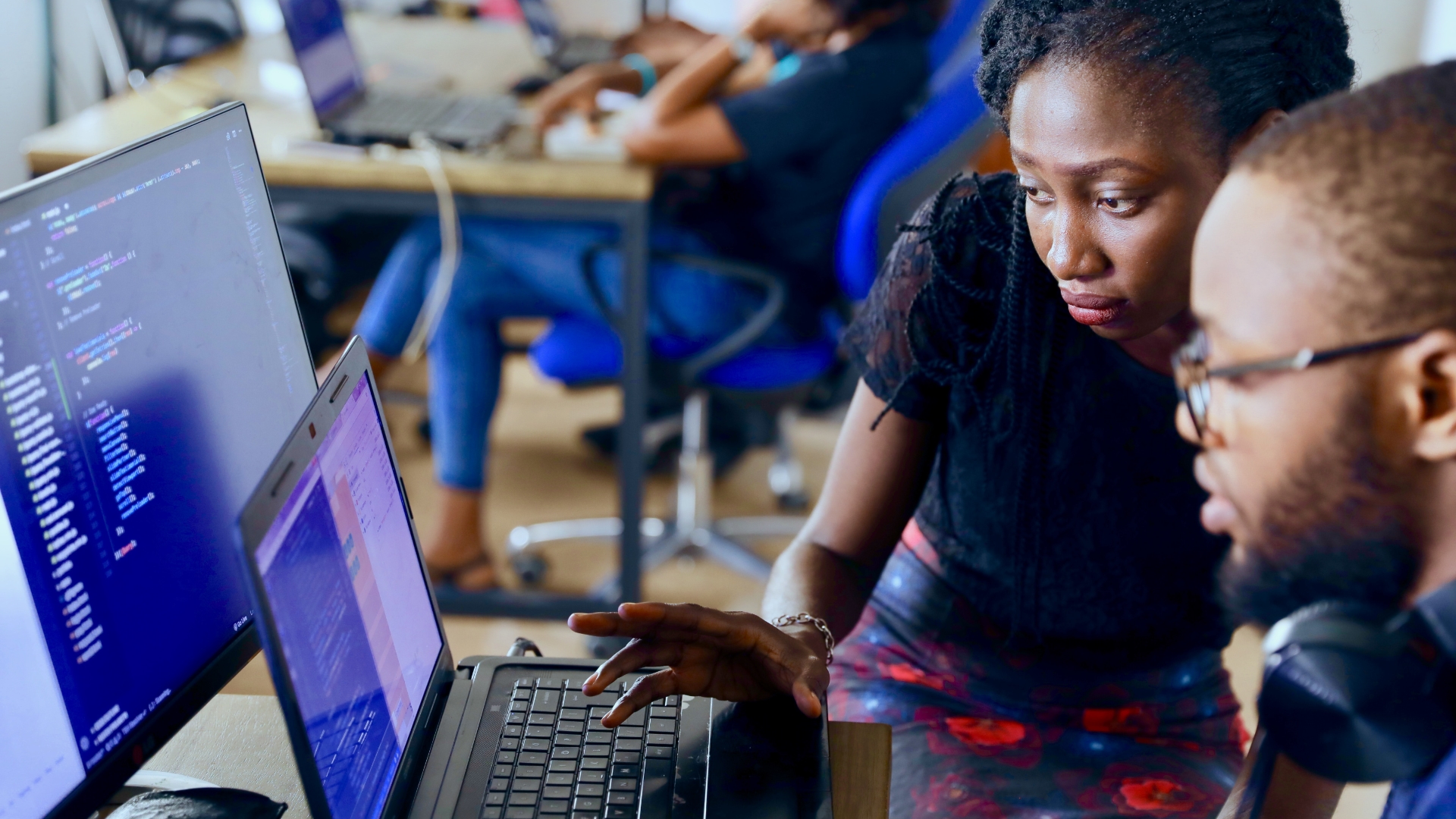 An African woman man from Lagos, Nigeria analyzing computer code on two computer screens. The woman’s hand seems to be preparing to type something on the keyboard.